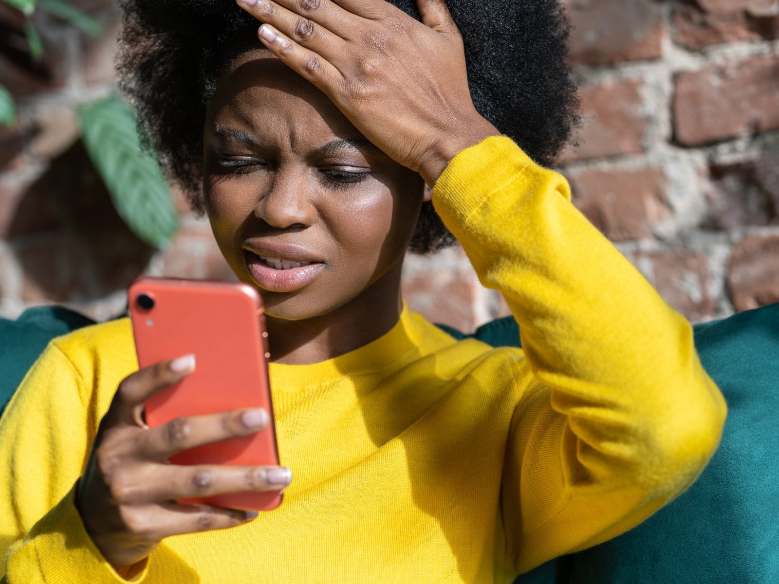 Confused Afro-American woman doing facepalm gesture, touching head with palm, look at phone